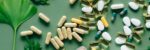 Flat lay of assorted pills and herbs on green surface, symbolizing health and wellness.